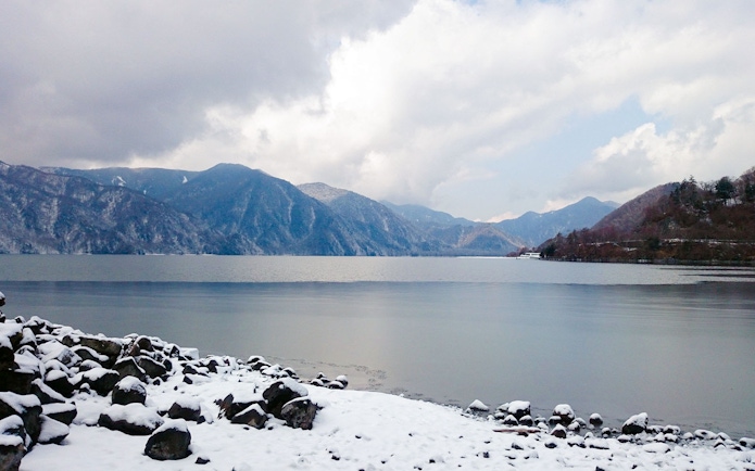 Snow-covered shore of Lake Chūzenji with mountain backdrop in Nikko.
