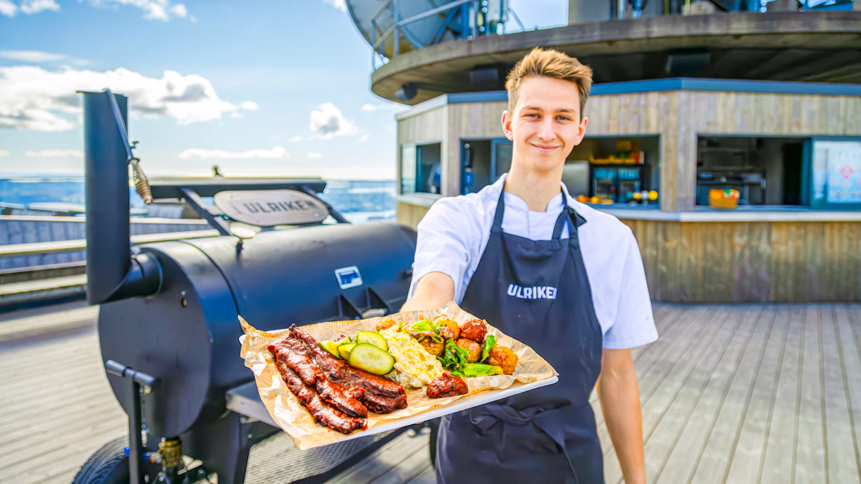 Server presenting a platter of grilled meats and vegetables at Skyskraperen Restaurant, Ulriken.