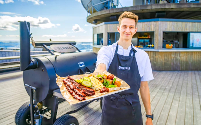 Server presenting a platter of grilled meats and vegetables at Skyskraperen Restaurant, Ulriken.