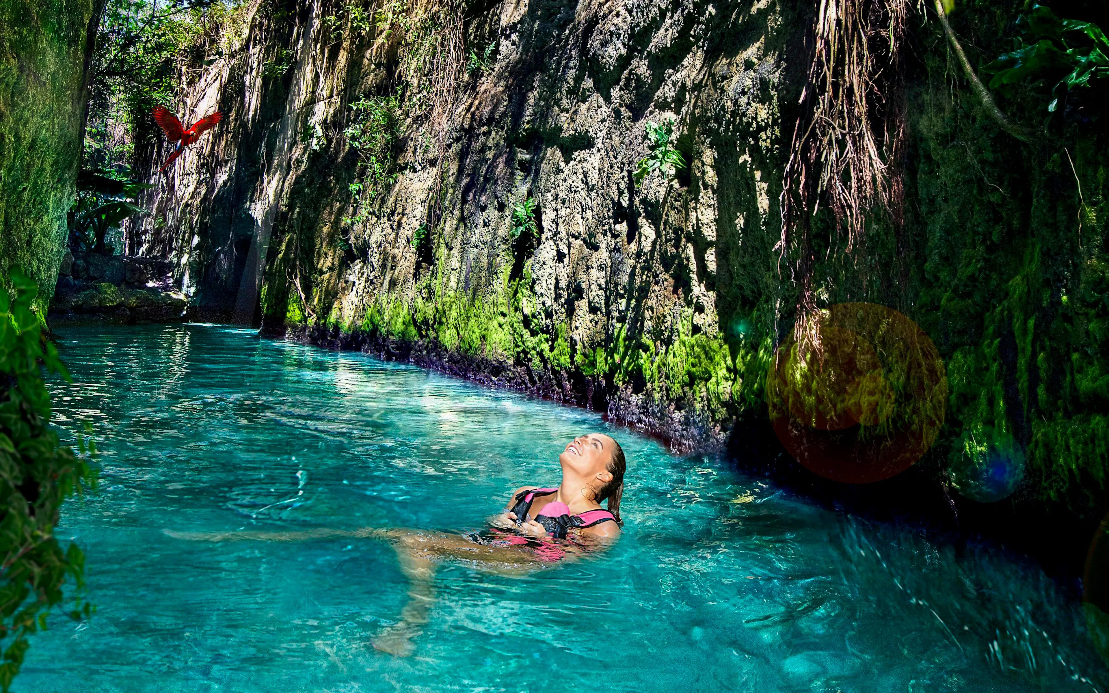 Floating in a turquoise river at Xcaret Park with lush greenery and a parrot overhead.