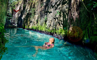 Floating in a turquoise river at Xcaret Park with lush greenery and a parrot overhead.