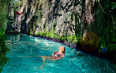 Floating in a turquoise river at Xcaret Park with lush greenery and a parrot overhead.