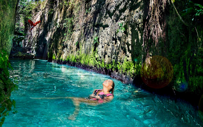 Floating in a turquoise river at Xcaret Park with lush greenery and a parrot overhead.