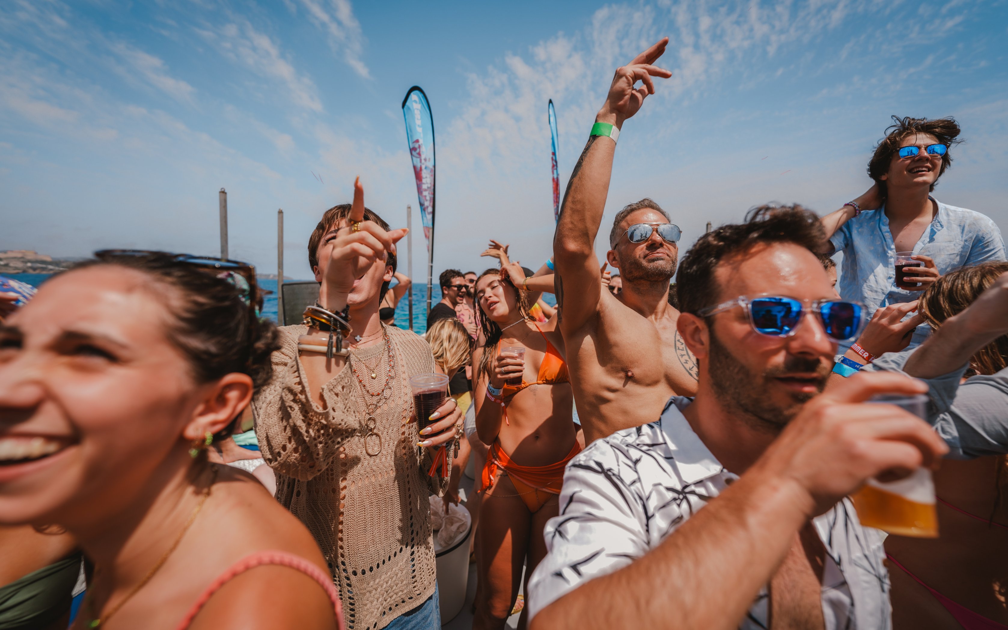 Tourists enjoying a lively Cruise Crush Boat Party under a clear blue sky.