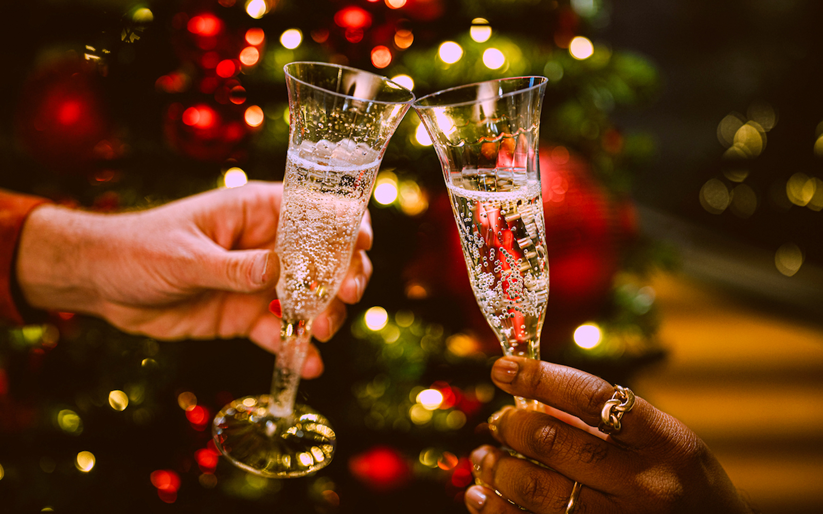 Champagne glasses clinking in front of festive lights on New Year’s Eve cruise in NYC.
