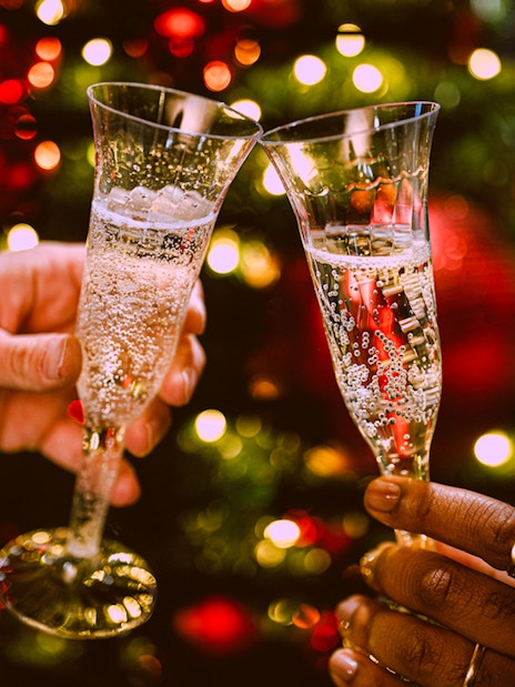 Champagne glasses clinking in front of festive lights on New Year’s Eve cruise in NYC.