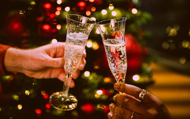 Champagne glasses clinking in front of festive lights on New Year’s Eve cruise in NYC.