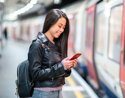 Woman smiling at phone on platform, waiting for JR Haruka Airport Express.