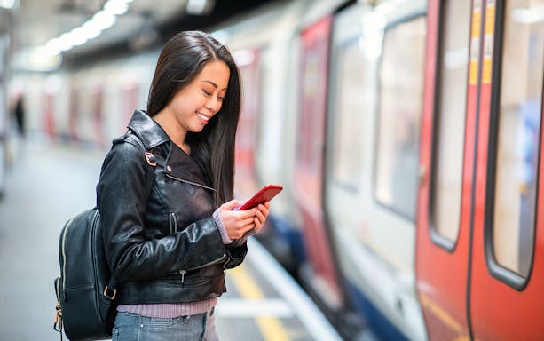Woman smiling at phone on platform, waiting for JR Haruka Airport Express.