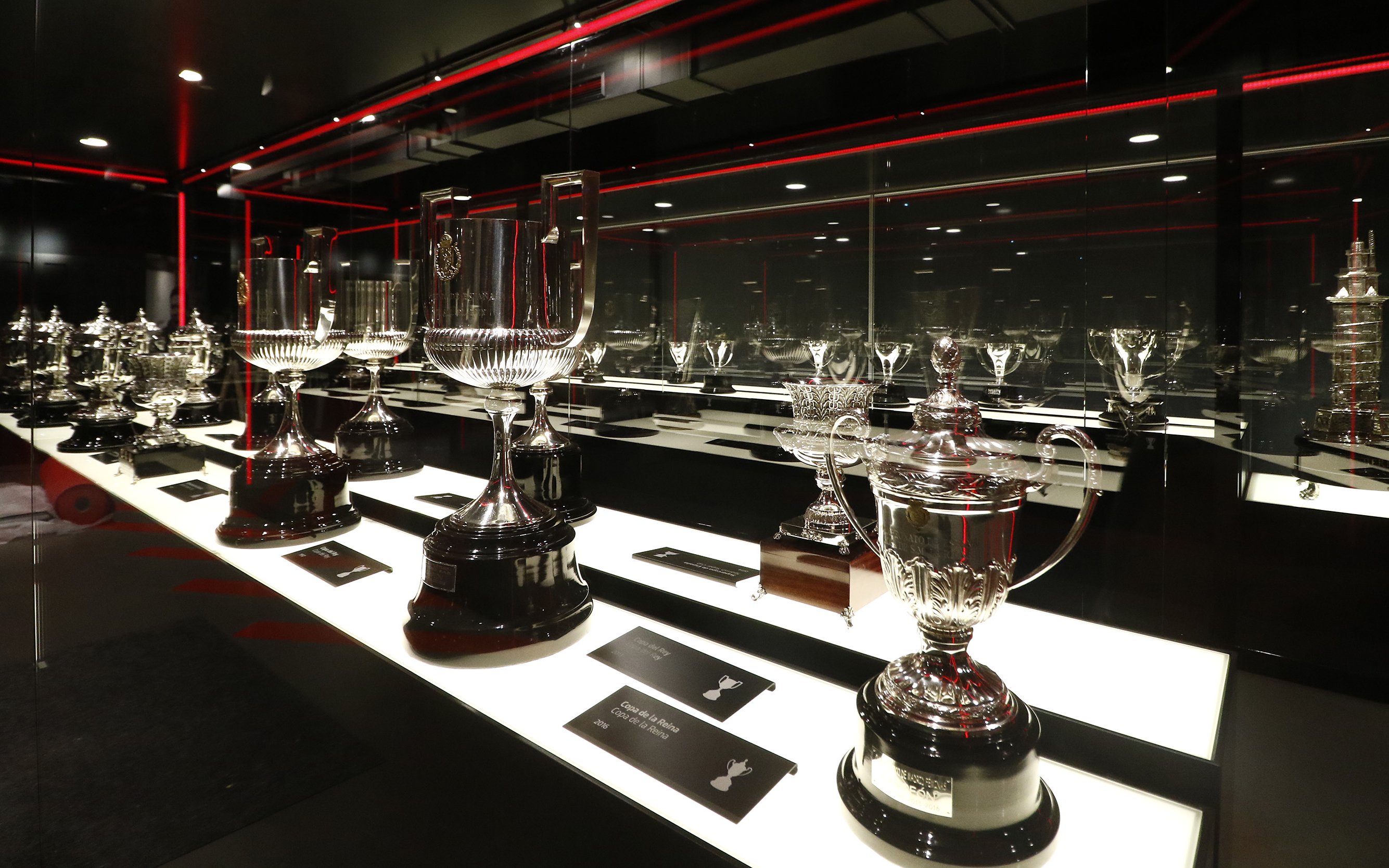 Atlético Madrid stadium museum trophy display with various silver cups.