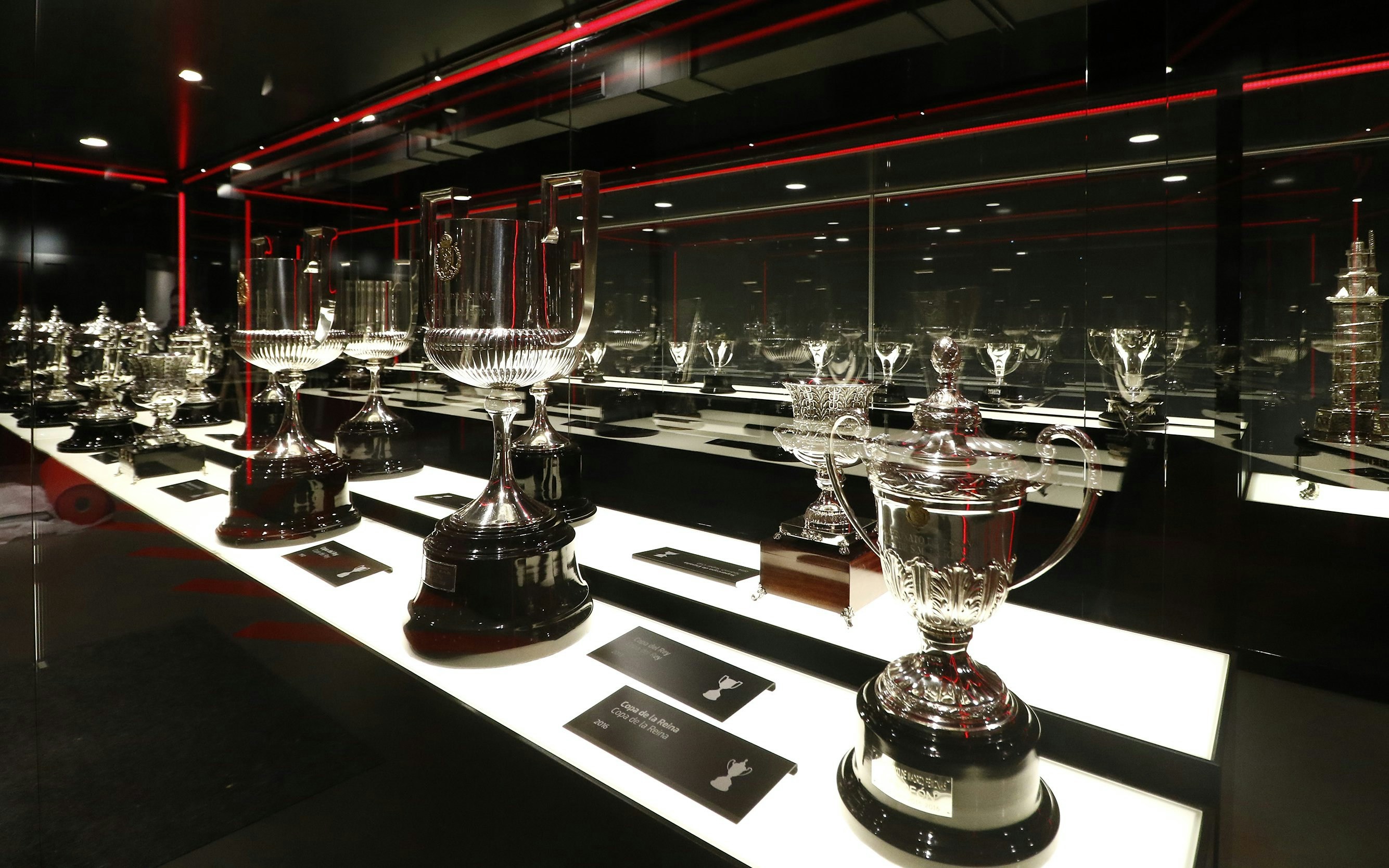 Atlético Madrid stadium museum trophy display with various silver cups.