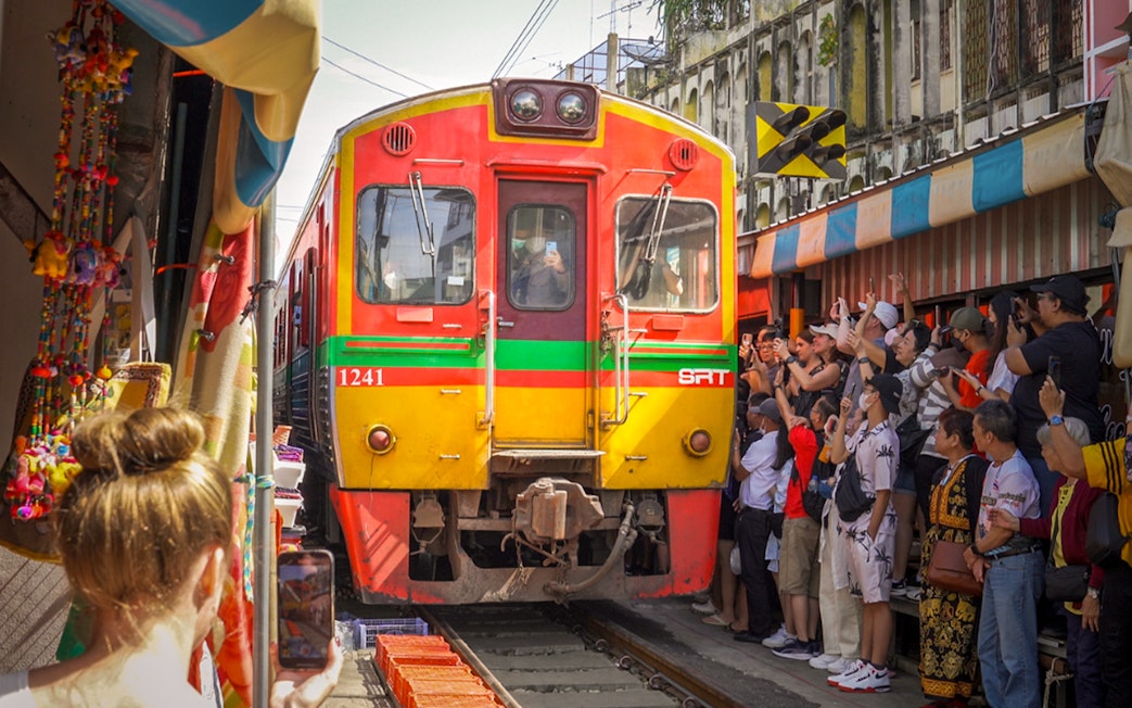 Train passing through Maeklong Railway Market with tourists taking photos, Bangkok tour.