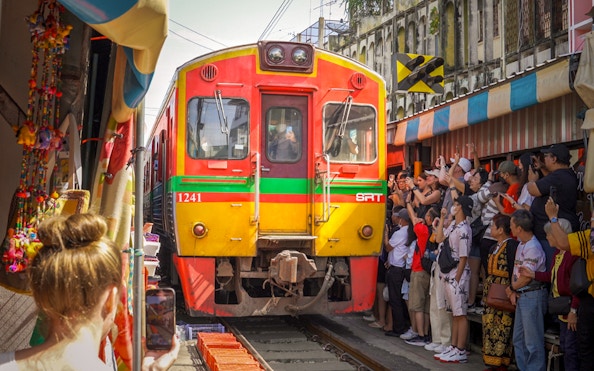 Train passing through Maeklong Railway Market with tourists taking photos, Bangkok tour.