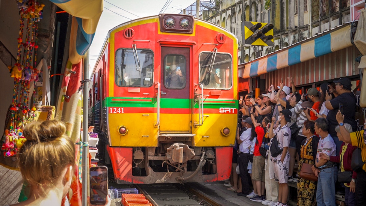 Train passing through Maeklong Railway Market with tourists taking photos, Bangkok tour.