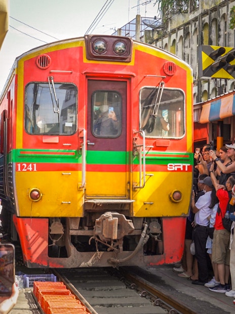 Train passing through Maeklong Railway Market with tourists taking photos, Bangkok tour.
