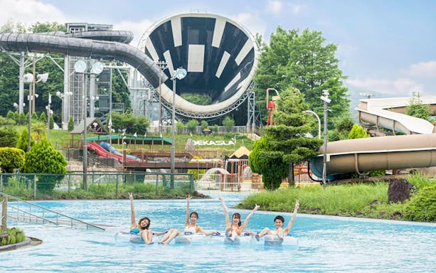 Visitors enjoying a lazy river at Tokyo Summerland with water slides in the background.