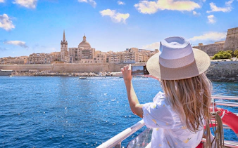 Tourist photographing Valletta skyline from a harbour cruise in Malta.