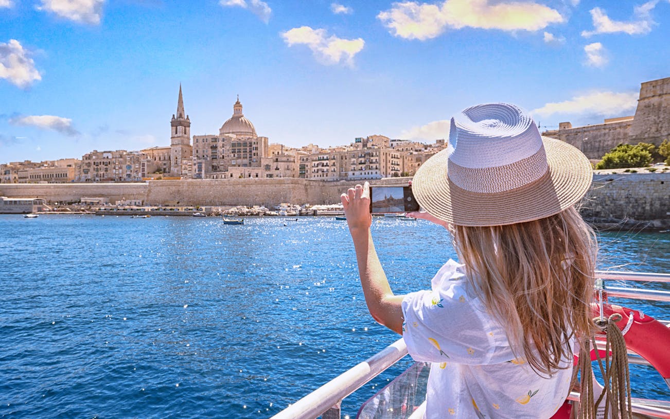 Tourist photographing Valletta skyline from a harbour cruise in Malta.