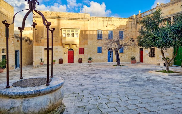 Historic courtyard in Mdina, Malta with colorful doors and ancient well.