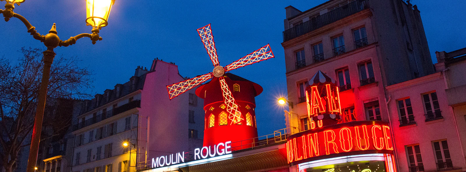 Moulin Rouge entrance with illuminated windmill and neon lights in Paris at night.