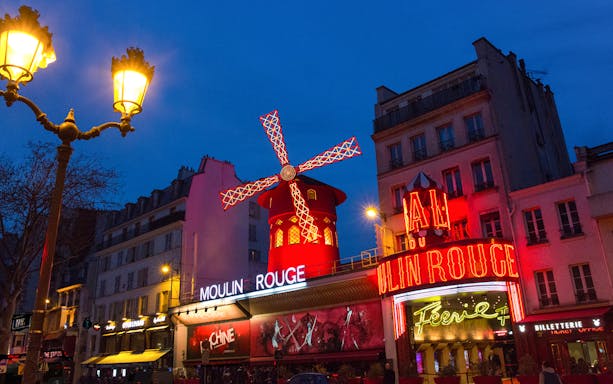 Moulin Rouge entrance with illuminated windmill and neon lights in Paris at night.