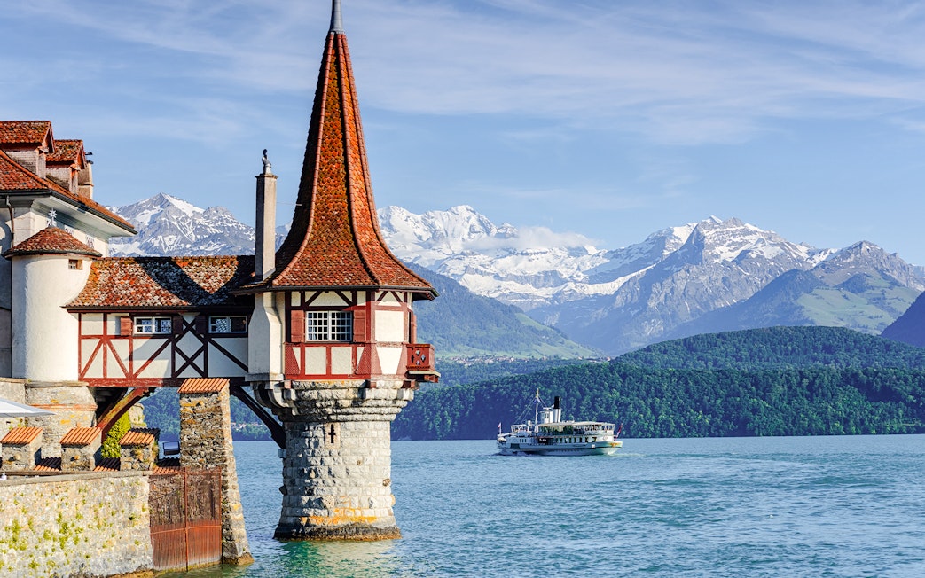 Historic castle tower by Lake Thun with boat and Alps in Bernese Highlands, Switzerland.