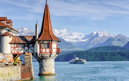 Historic castle tower by Lake Thun with boat and Alps in Bernese Highlands, Switzerland.