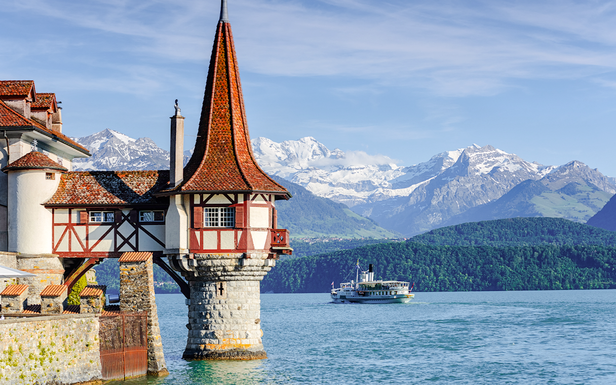 Historic castle tower by Lake Thun with boat and Alps in Bernese Highlands, Switzerland.