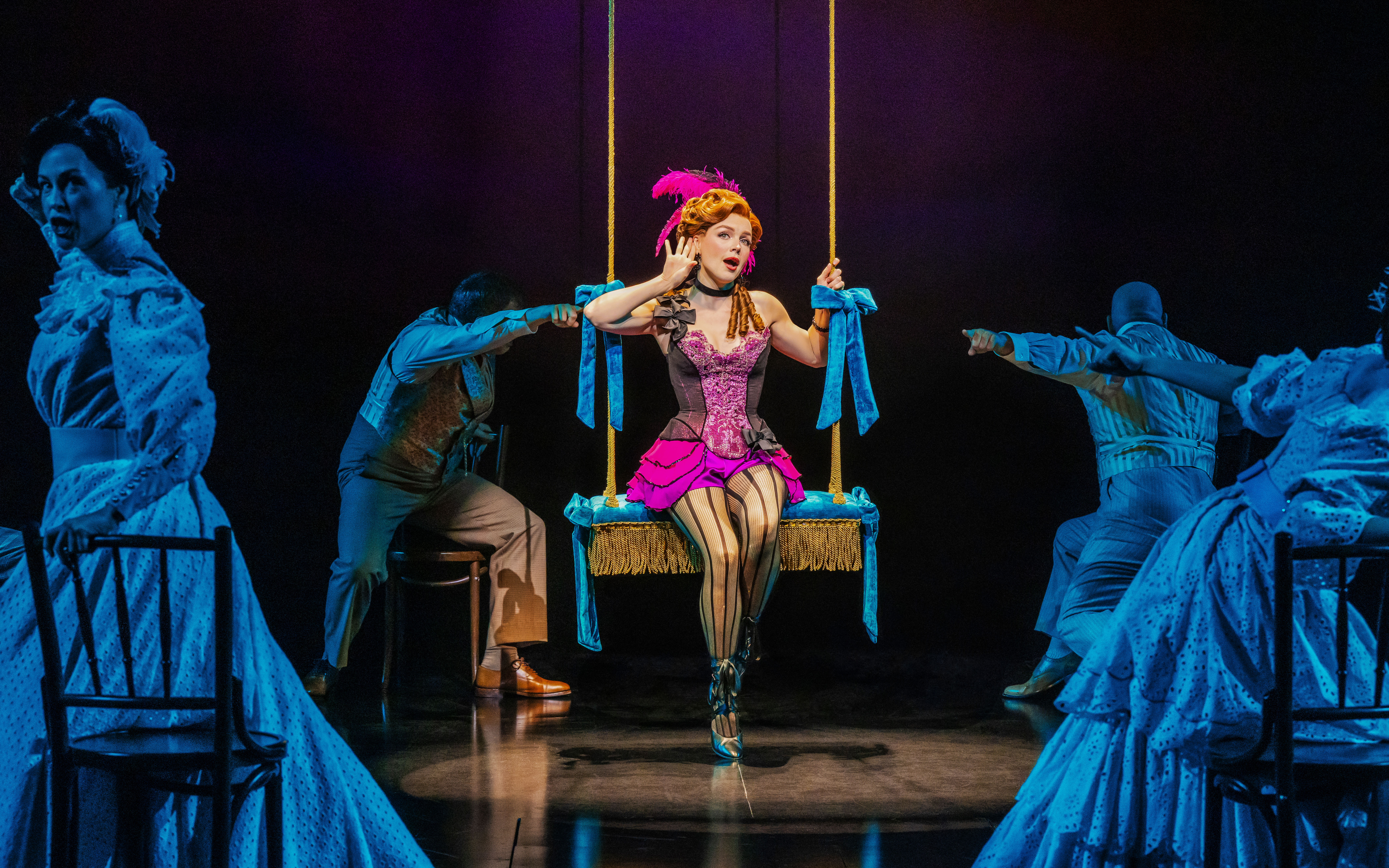Performer on swing in Ragtime musical scene with actors in period costumes.