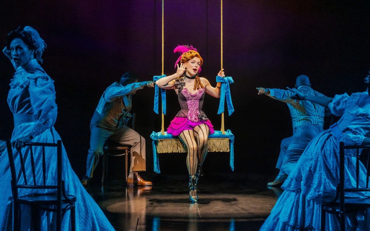 Performer on swing in Ragtime musical scene with actors in period costumes.