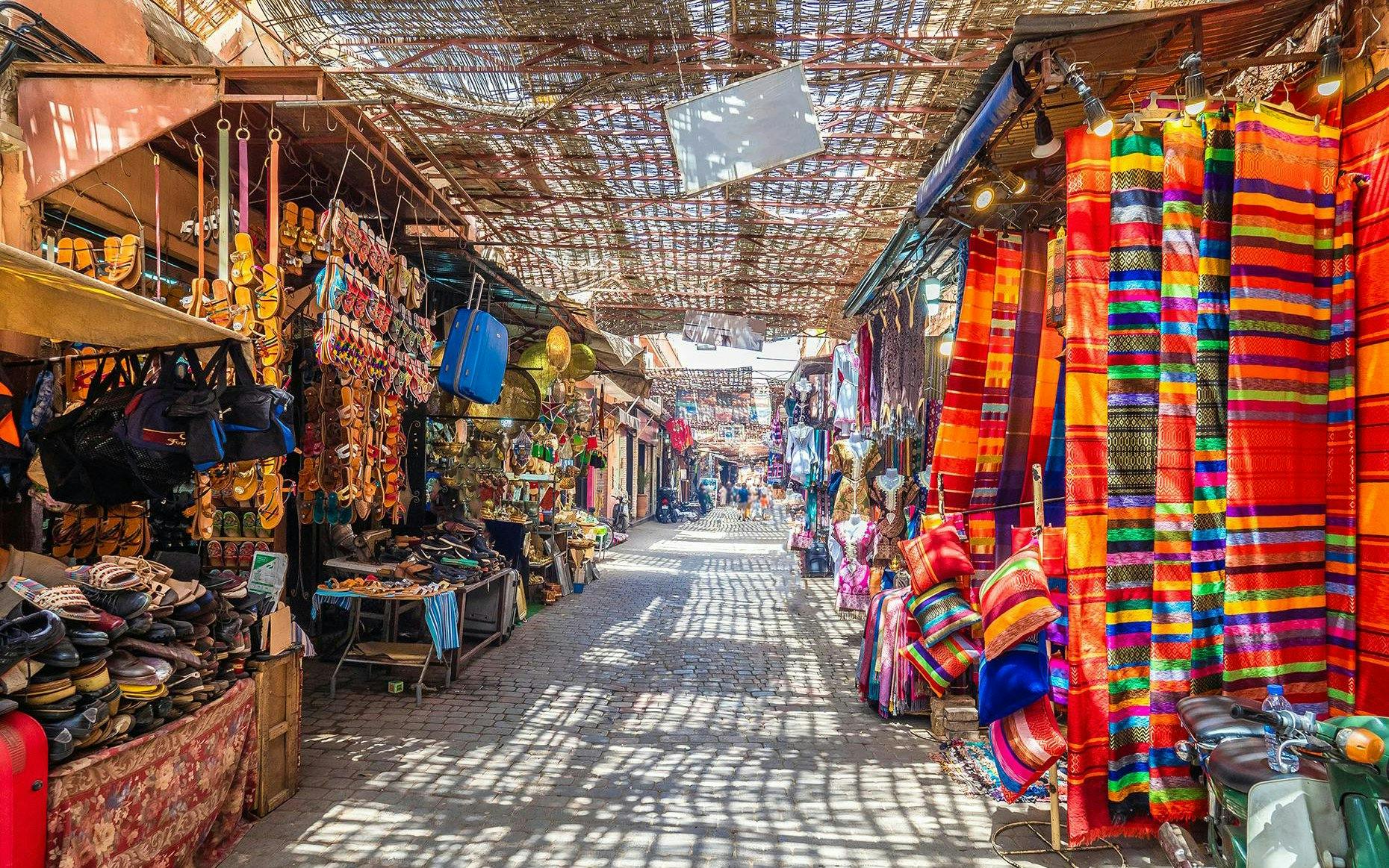 Marrakech market with colorful textiles and sandals displayed, part of Agadir full-day city tour.