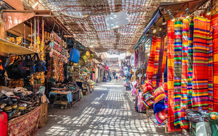 Marrakech market with colorful textiles and sandals displayed, part of Agadir full-day city tour.