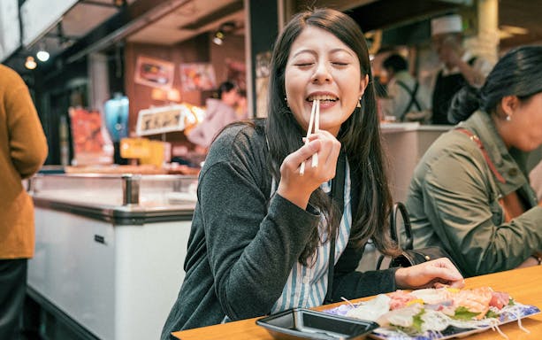Woman enjoying sushi with chopsticks on a Japanese street food tour in Shibuya.