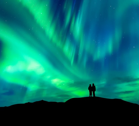 Silhouette of a couple watching the aurora borealis in a starry night sky.
