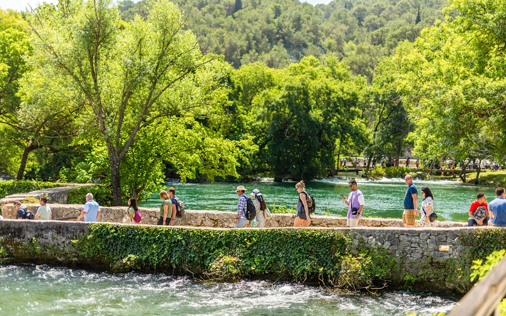 Visitors walking along a stone path by the river at Krka Waterfalls, Split day trip.