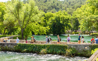 Visitors walking along a stone path by the river at Krka Waterfalls, Split day trip.