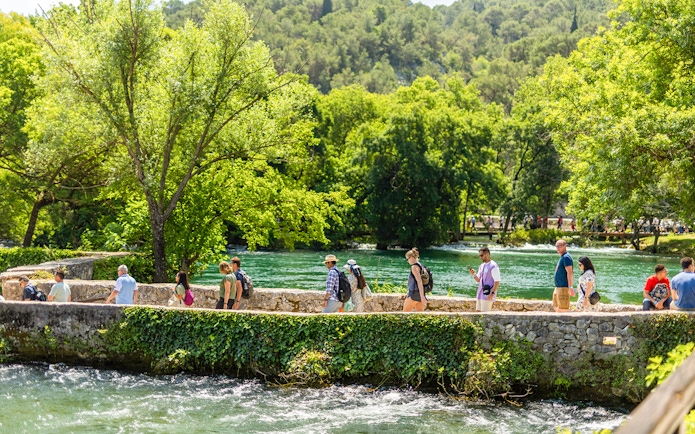 Visitors walking along a stone path by the river at Krka Waterfalls, Split day trip.