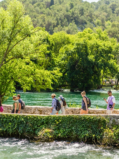 Visitors walking along a stone path by the river at Krka Waterfalls, Split day trip.