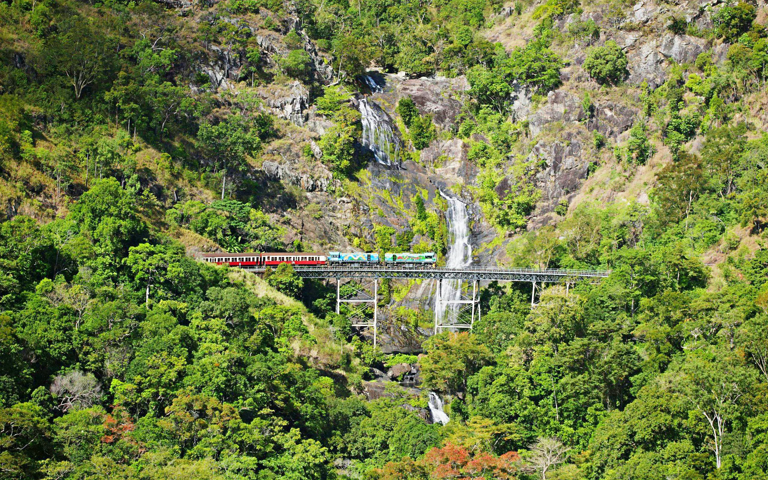 Kuranda Scenic Rail crossing a bridge with a waterfall in the background.