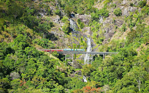 Kuranda Scenic Rail crossing a bridge with a waterfall in the background.