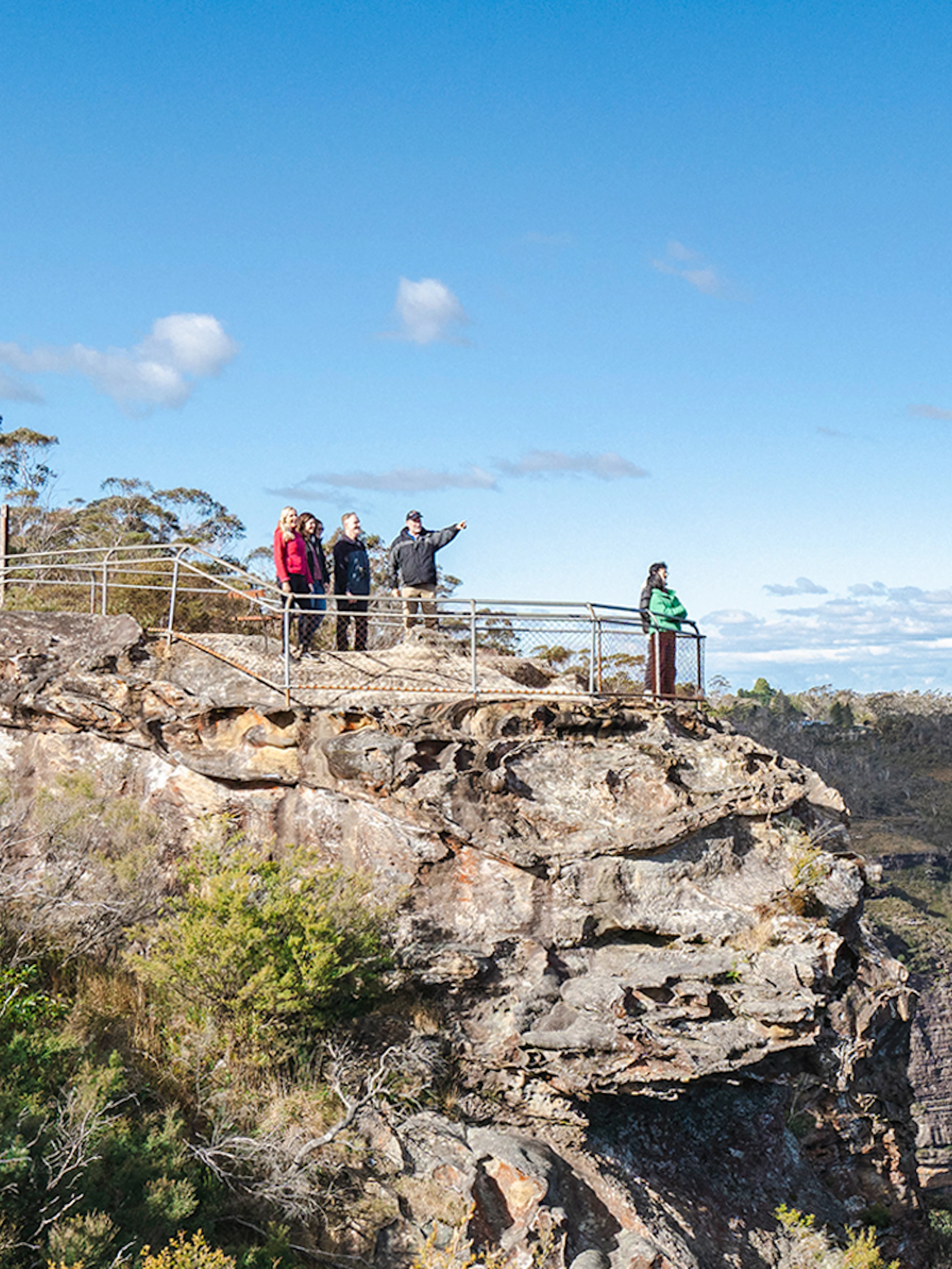 Tour group with guide at Blue Mountains viewpoint, overlooking scenic cliffs and forest.