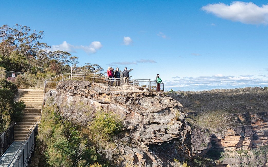 Tour group with guide at Blue Mountains viewpoint, overlooking scenic cliffs and forest.