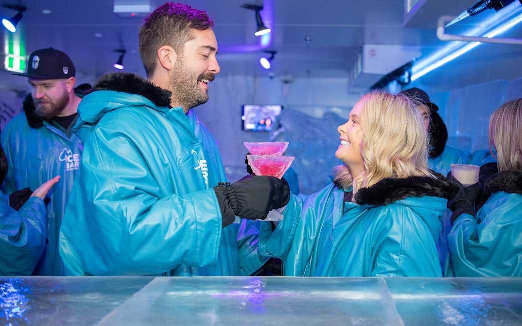 Couple enjoying cocktails at IceBar Surfers Paradise in blue parkas.