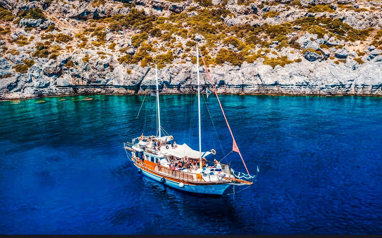 Sailing boat on clear blue waters near rocky coast, Rhodes All-Inclusive Cruise.