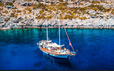 Sailing boat on clear blue waters near rocky coast, Rhodes All-Inclusive Cruise.