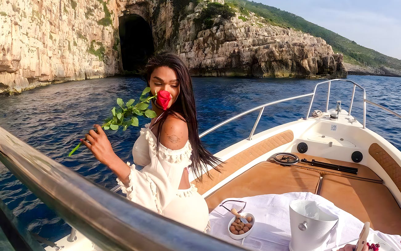 Boat approaching the Cave of Haxhi Ali, Albania, with a person holding a rose.