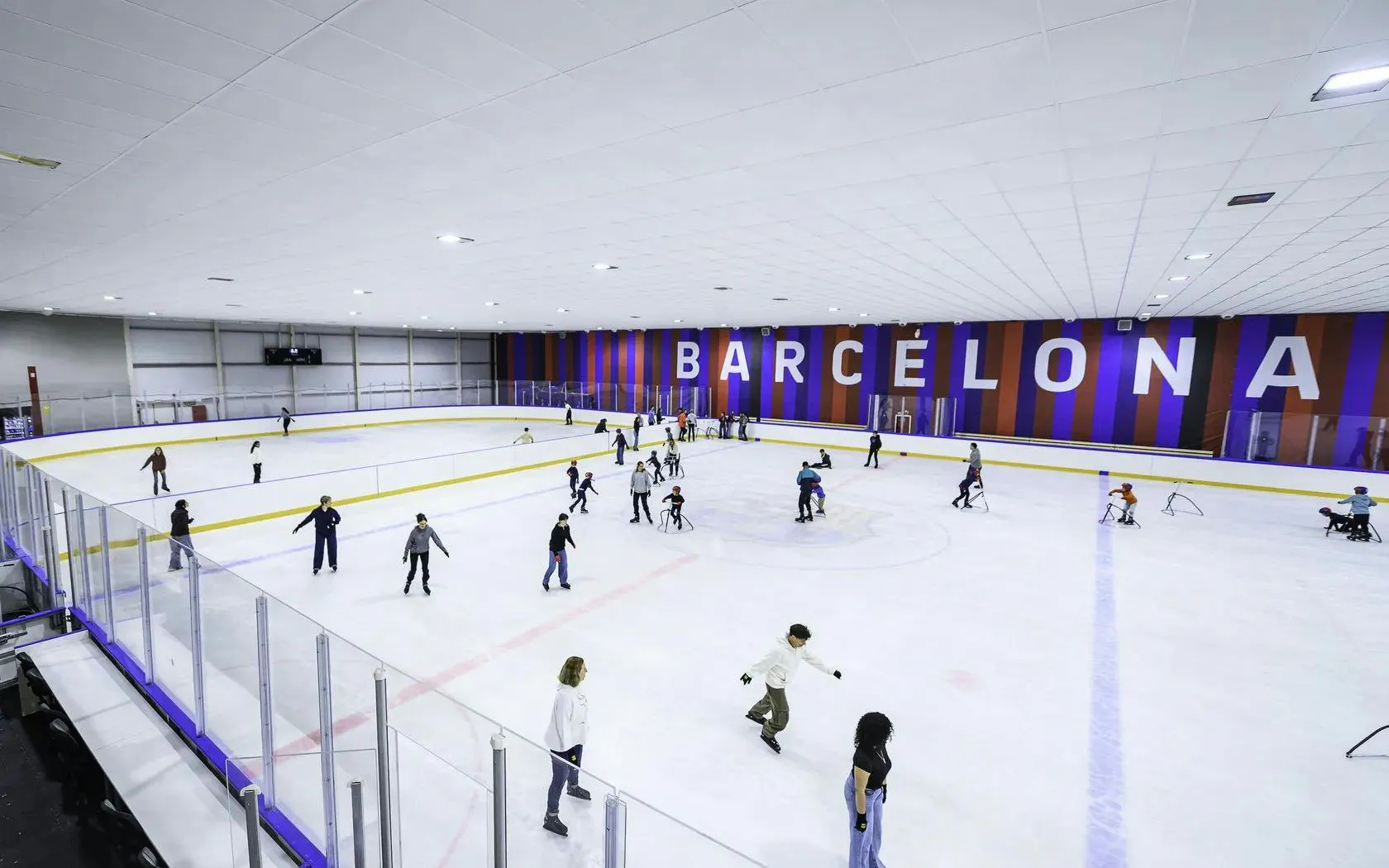 People ice skating at FC Barcelona Ice Rink with "Barcelona" on the wall.