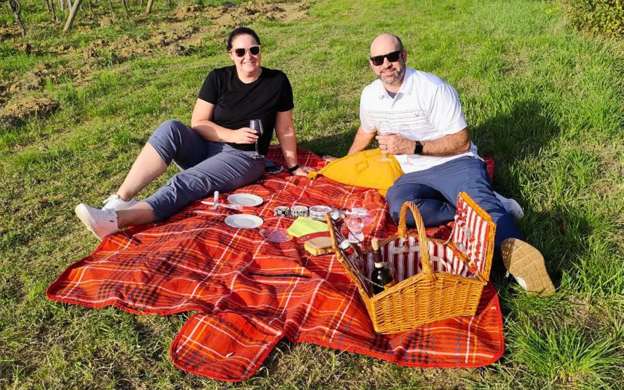 Couple enjoying aperitivo picnic on a red blanket in Chianti vineyard.