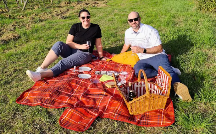 Couple enjoying aperitivo picnic on a red blanket in Chianti vineyard.