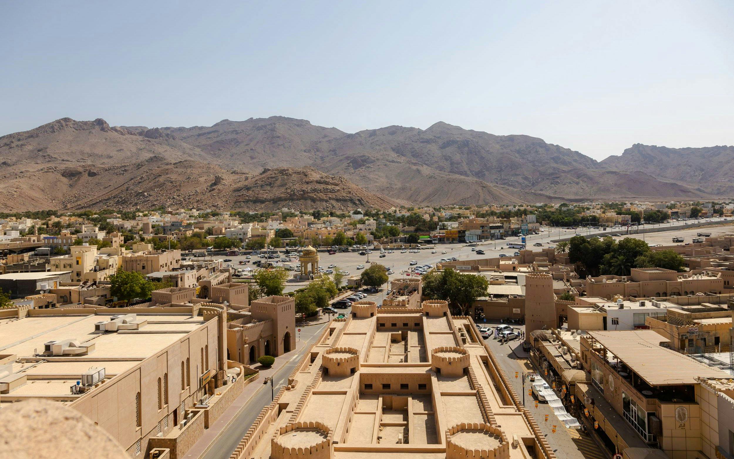 Aerial view of Nizwa Fort with surrounding cityscape and mountains in Oman.